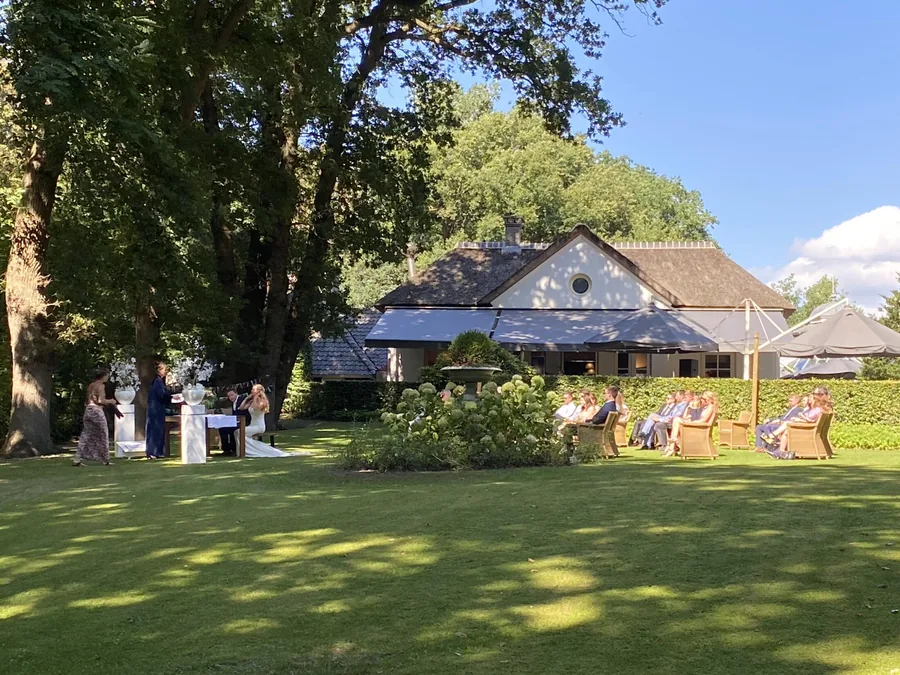 Gasten zitten op stoelen in het gras voor het Theehuis tijdens een ceremonie