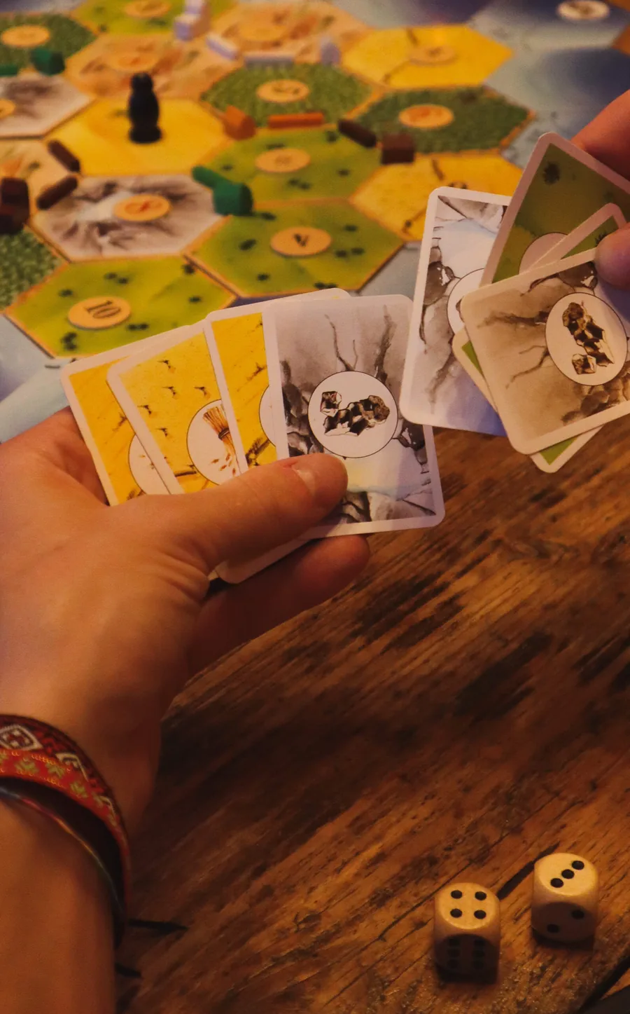 Handen met speelkaarten boven een bordspel op een houten tafel