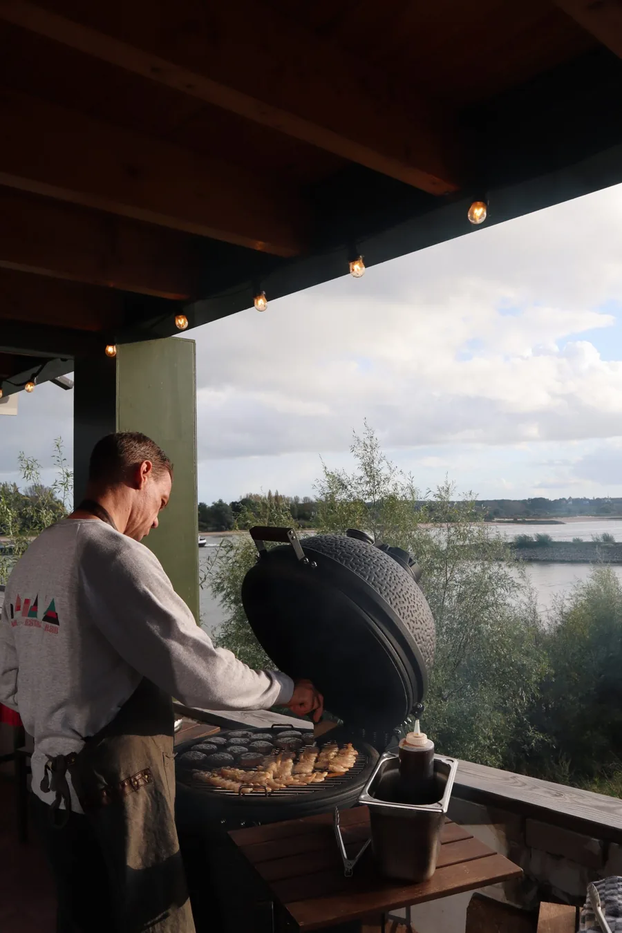 Iemand staat te barbecueën op de veranda, met uitzicht over de Waal