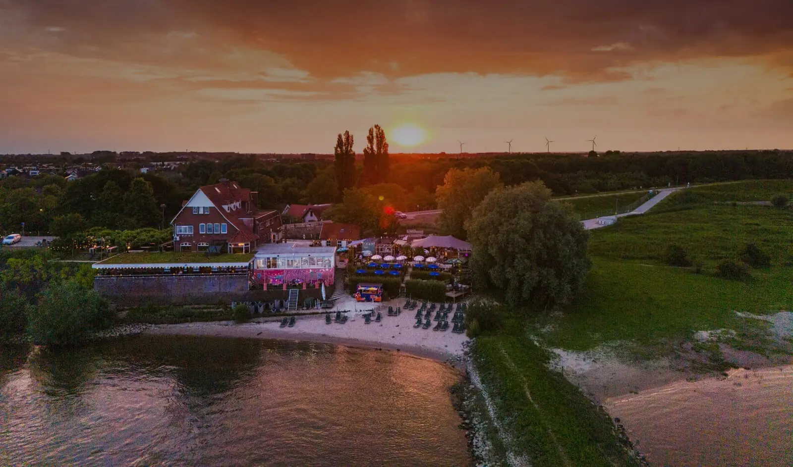 Baiana aan de Waal bij zonsondergang, gezien vanuit de lucht: het roze gebouw, het terras en het strand langs de rivier