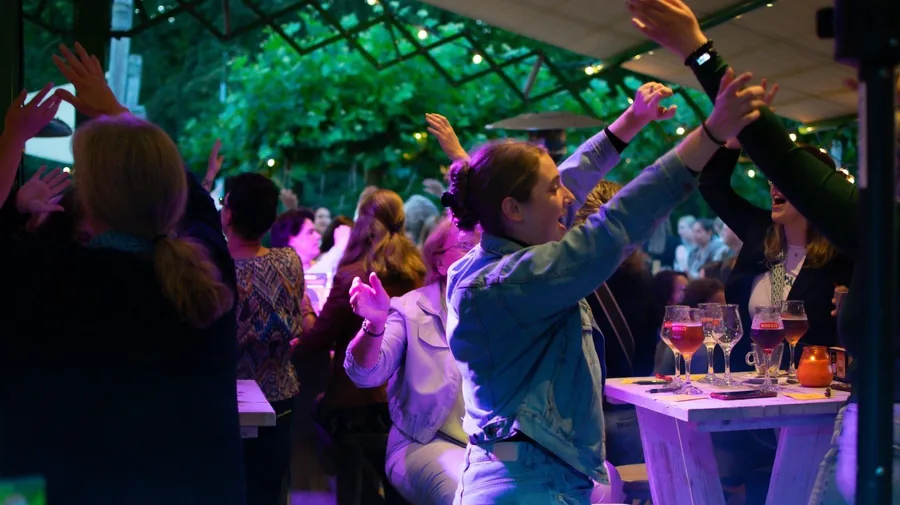 Gasten dansen met de armen omhoog onder gekleurde lampjes op een feest