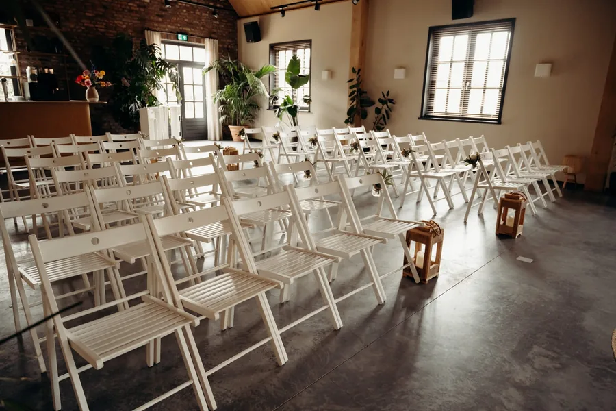 Rijen witte stoelen met lantaarns in de zaal, gezien vanaf de zijkant
