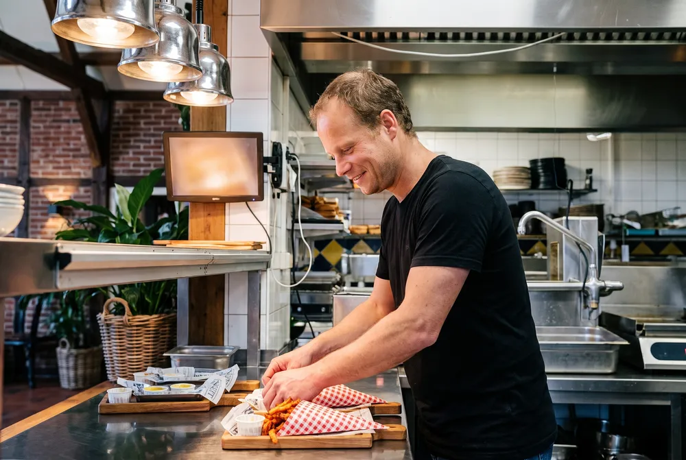Pim Hamburg werkt bij de pass in de keuken, met een klein scherm naast de doorgeef