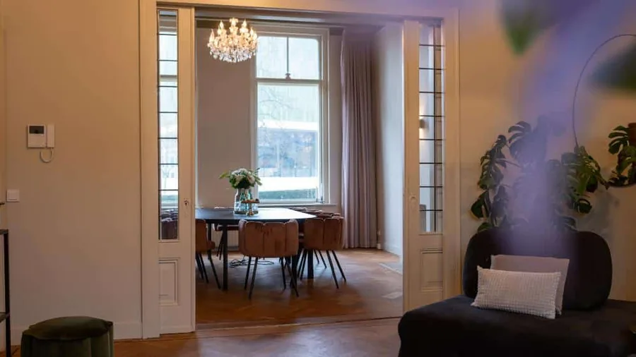 Een zaal met een kroonluchter en een ovale tafel, gezien door de openslaande deuren