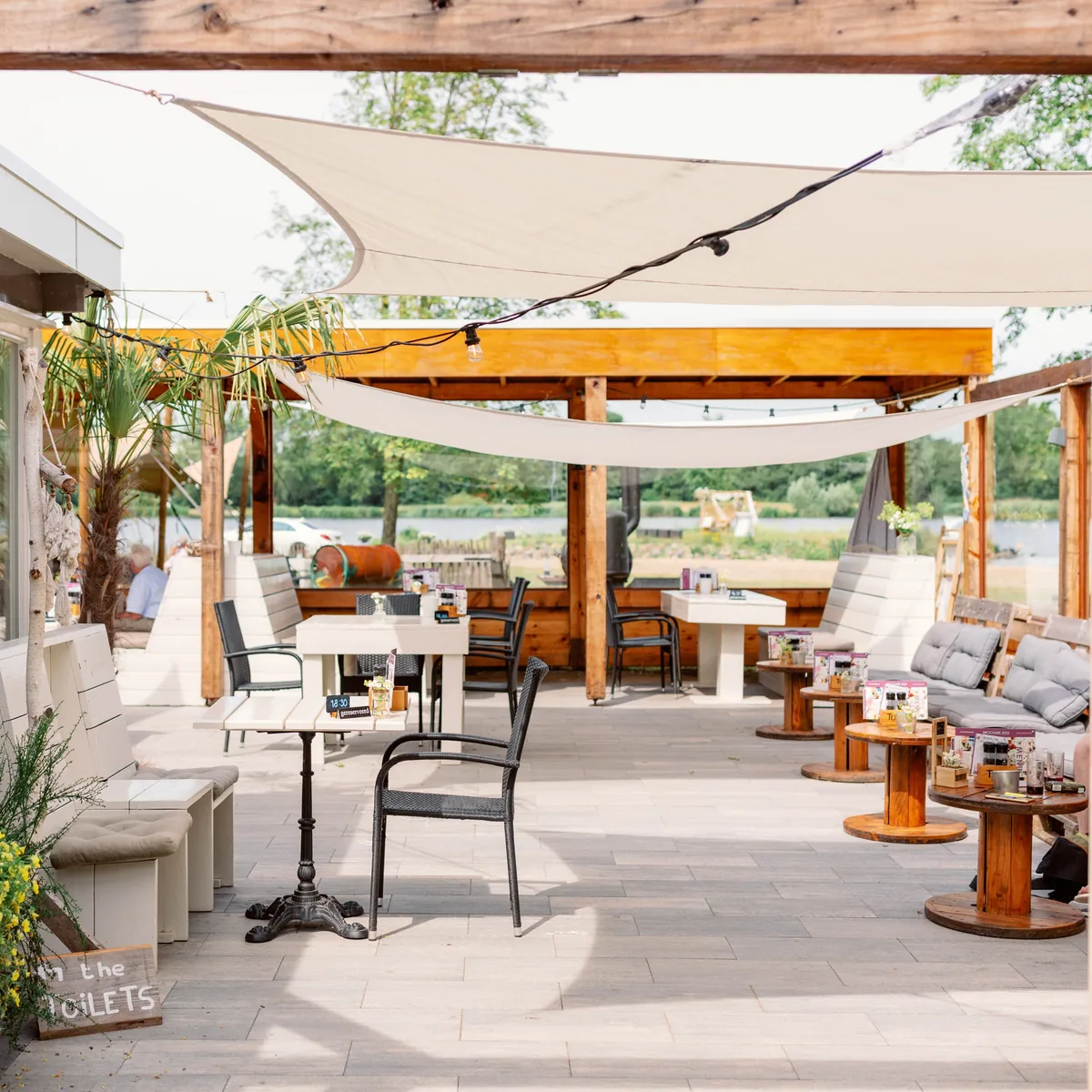 Het loungeterras van Breezze onder witte zeilen, met uitzicht over het water