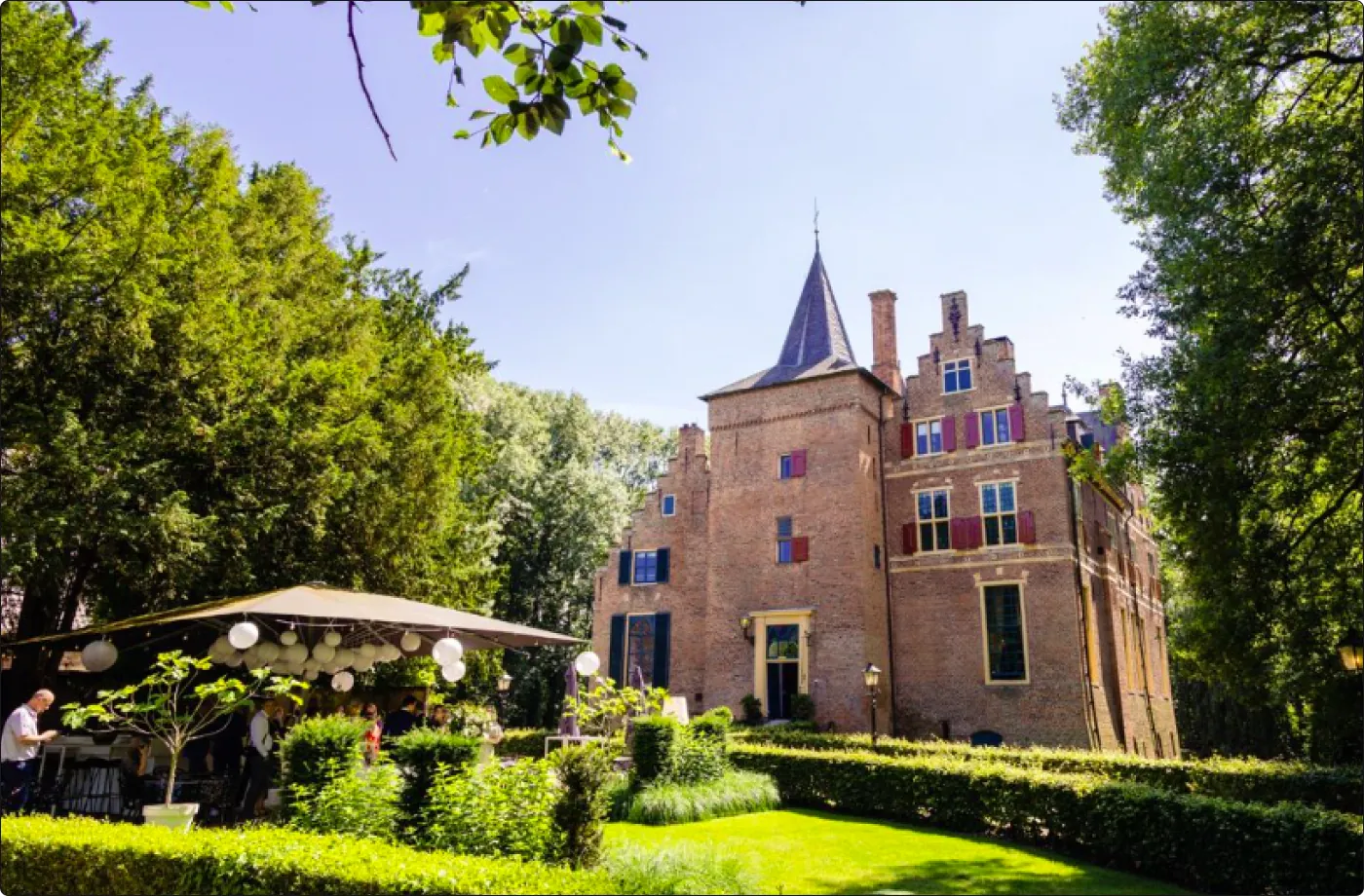 Gasten onder een parasol in de tuin van Kasteel Wijenburg op een zomerse dag