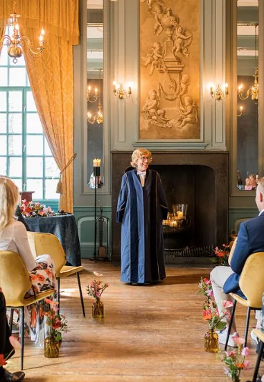 Een ceremonie in de zaal van Kasteel Wijenburg, met gouden gordijnen en gasten op fluwelen stoelen