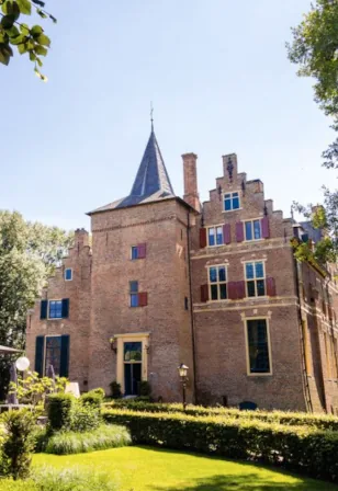 De bakstenen gevel en toren van Kasteel Wijenburg tegen een blauwe lucht