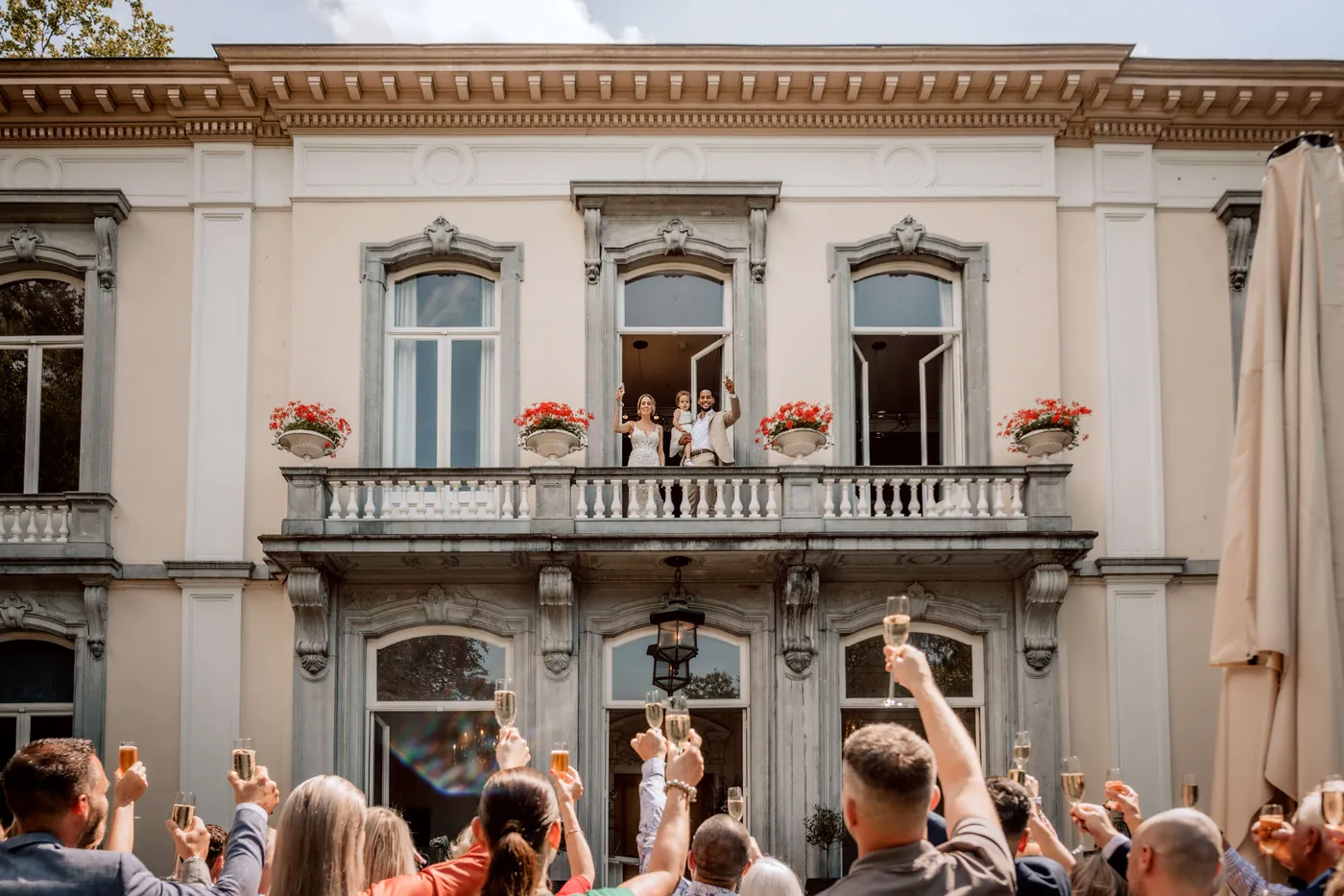 Gasten toosten voor de gevel van het landhuis terwijl het bruidspaar op het balkon staat