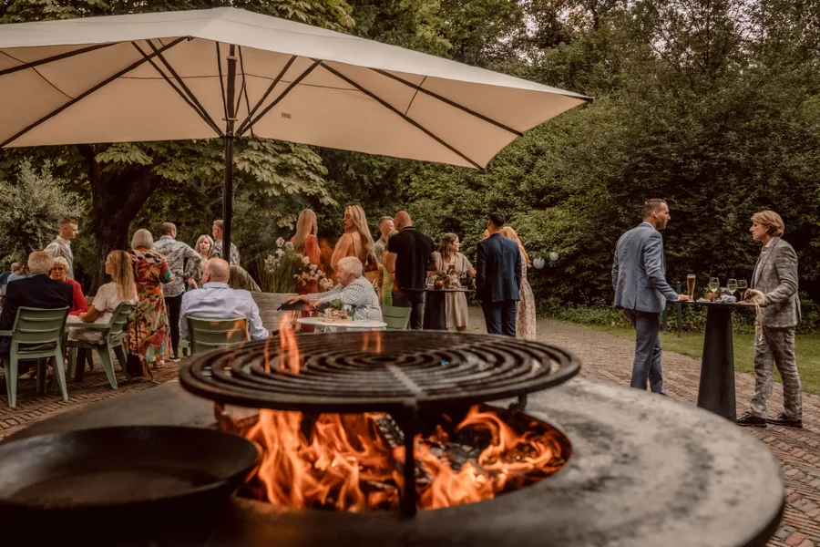 Gasten staan met een drankje rond een vuurschaal in de tuin van het landgoed